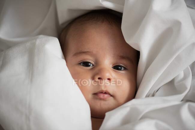 Top view of cute infant wrapped in white fabric looking at camera at home — Stock Photo