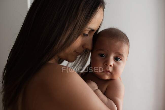 Adult woman hugging and gently touching cute infant while resting at home together — Stock Photo
