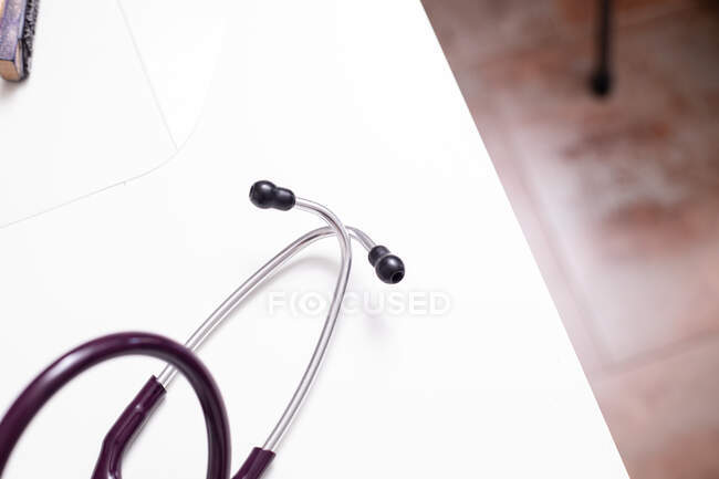 Stéthoscope placé sur un bureau blanc près du livre sur le lieu de travail médical moderne en clinique légère après consultation et examen du patient — Photo de stock