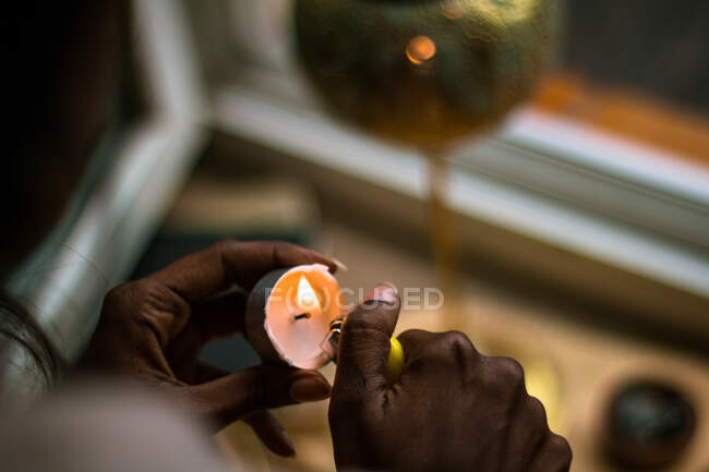 Crop anonymous ethnic female shaman with lighter lightning tea candle while preparing for spiritual ritual — Stock Photo