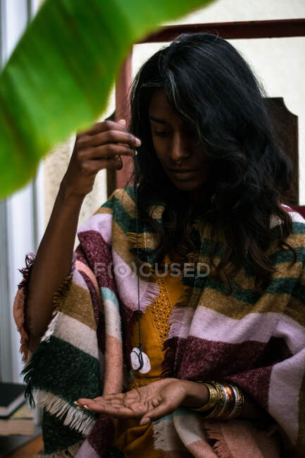Jovem xamã étnico feminino em roupa tradicional segurando cristal pingente e realizando ritual misterioso — Fotografia de Stock