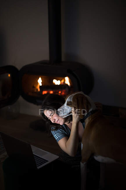 Von oben glückliche Frau sitzt auf dem Boden im dunklen Wohnzimmer mit Kamin und umarmt Weihe, während Video auf Laptop zusammen — Stockfoto