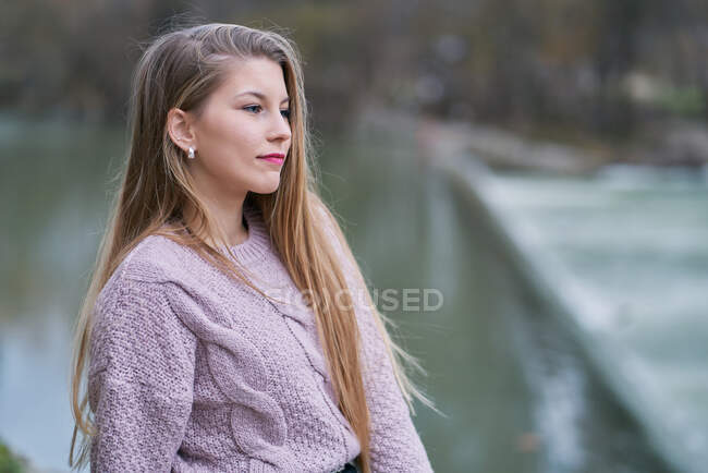 Pensiva donna bionda che indossa maglione viola chiaro guardando lontano contro lo sfondo sfocato — Foto stock