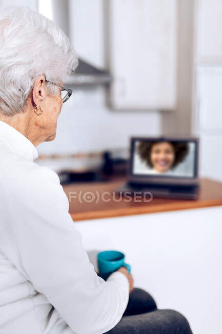 Старша жінка п'є чай і розмовляє з дочкою на ноутбуці — стокове фото