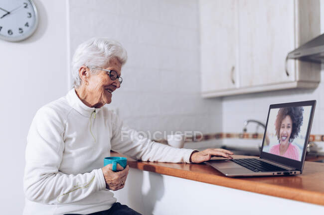 Старшая женщина пьет чай и разговаривает с дочерью на ноутбуке — стоковое фото