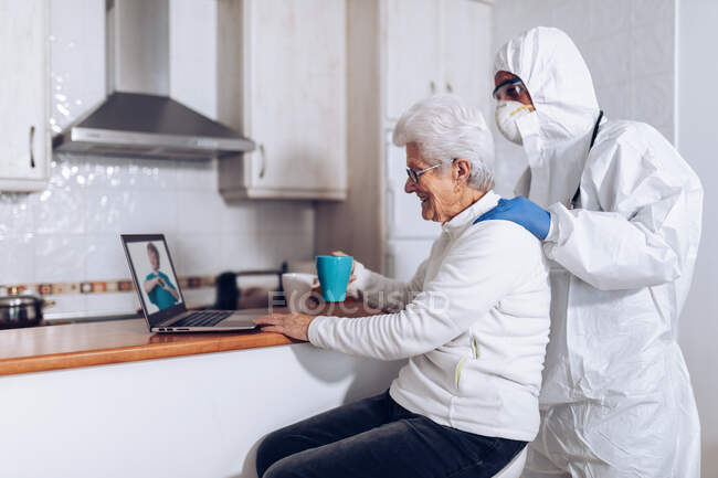 Senior woman with home care assistant enjoying video conversation via laptop — Stock Photo