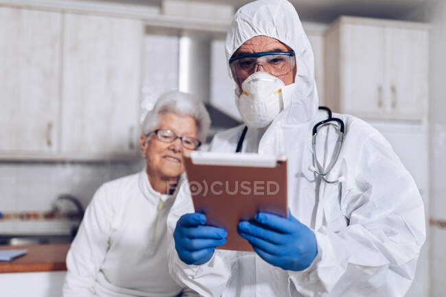Médico explicando información médica al paciente mayor en casa durante la cuarentena del coronavirus - foto de stock