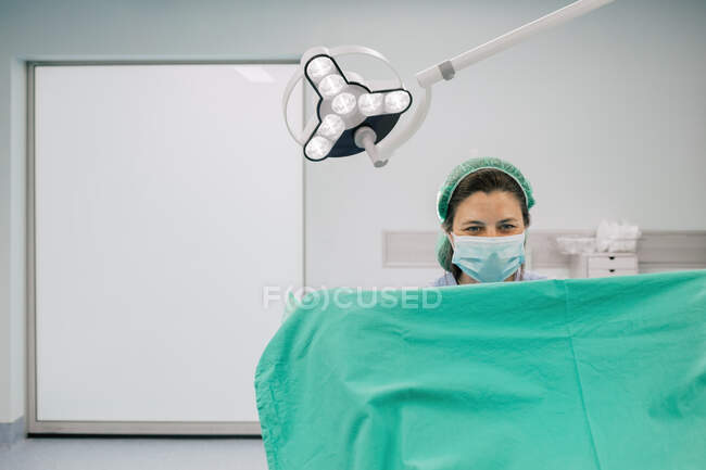 Doctora en uniforme azul y máscara estéril examinando paciente irreconocible en silla ginecológica en clínica de fertilidad - foto de stock