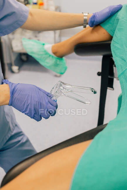 Безликі жінки-лікар в блакитних рукавичках і уніформі з пластиковим гінекологічним дзеркалом, що вивчає анонімного пацієнта в обкладинках взуття, лежачи на стільці в клініці фертильності — стокове фото