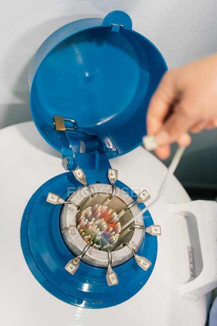 Неузнаваемый человек берет кабель с пластиковым разъемом из открытого криогенного резервуара с разноцветными деталями и фиксирует на голубой крышке в лаборатории — стоковое фото