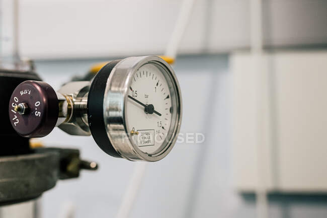Pressure gauge with round dial with different values and plastic black pointer installed near to large white hosepipe in clinic — Stock Photo