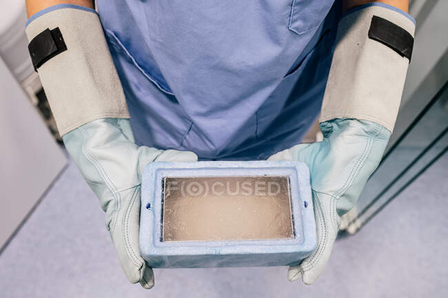Vue du dessus du médecin anonyme dans des gants de protection portant boîte cryogénique avec ovule congelé tout en travaillant dans le laboratoire de la clinique de fertilité moderne — Photo de stock