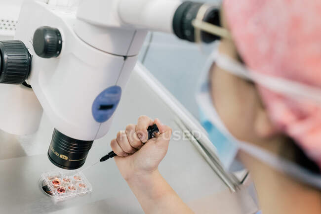 From above cropped unrecognizable doctor hand injecting ovum on Petri dish and examining cell through microscope in laboratory of modern fertility clinic — Stock Photo