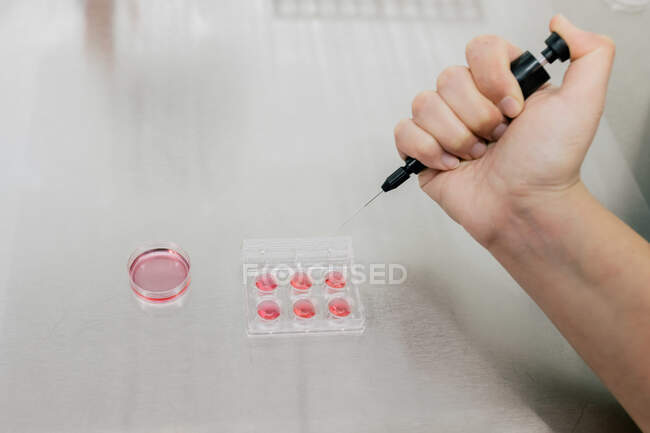 Von oben anonymer Arzt mit Injektor, um während der Arbeit im modernen Labor der Klinik gut Platte mit roter Flüssigkeit zu füllen — Stockfoto