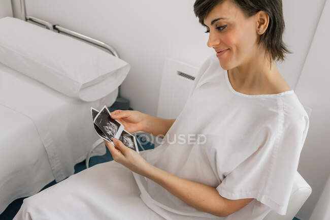 D'en haut femelle enceinte inspectant l'image d'échographie tout en étant assis dans une chaise dans la salle de la clinique de fertilité moderne — Photo de stock