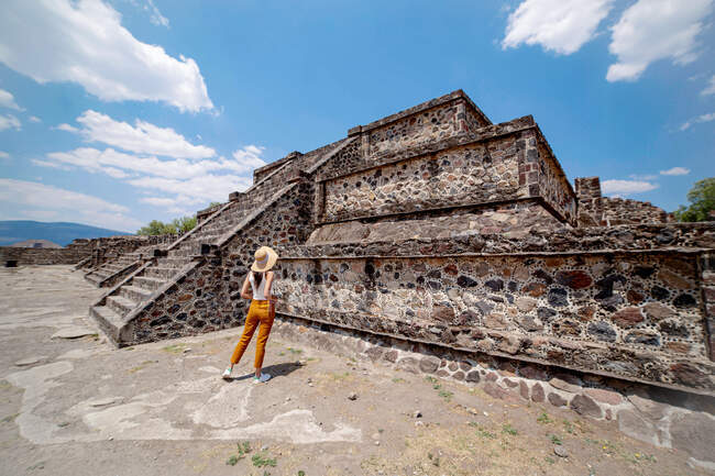 Vista posteriore di viaggiatore femminile anonimo indossando vestiti casual colorati e cappello alla moda in piedi vicino all'antico tempio nel soleggiato Messico — Foto stock