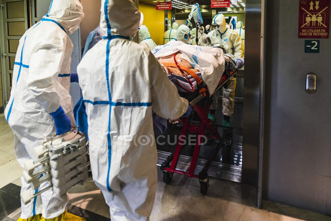 Gruppe unkenntlich gemachter Ärzte trägt Schutzuniform, während sie Patienten mit Virus aus dem Aufzug ins Krankenhaus bringen — Stockfoto