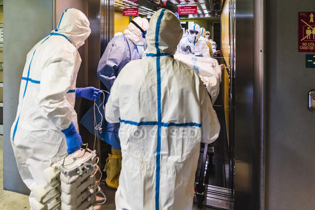Gruppo di medici irriconoscibili che indossano un'uniforme protettiva mentre prendono il paziente con il virus dall'ascensore in ospedale — Foto stock