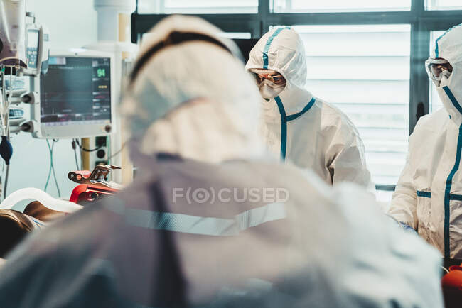 Médecins professionnels méconnaissables en uniformes de protection et masques prenant soin du patient infecté par le virus alors qu'il se tenait dans la salle d'opération de l'hôpital moderne — Photo de stock