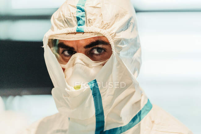 Портрет серйозного професійного лікаря в захисній формі і масці, що стоїть в сучасній операційній кімнаті і дивиться на камеру — стокове фото