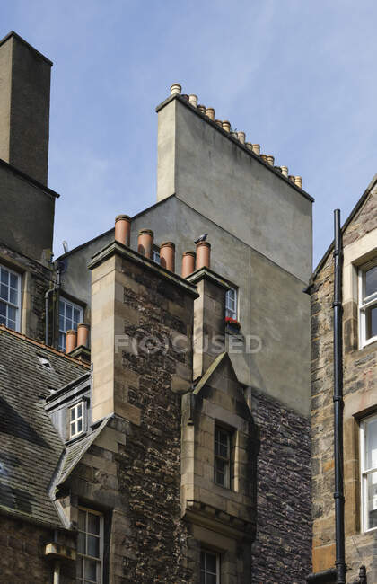 De baixo da velha casa de vários andares cinza-clara e marrom com janelas e chaminés localizada na rua da cidade no dia ensolarado com céu azul — Fotografia de Stock