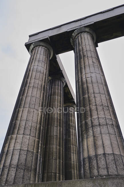From below of high ancient light brown ribbed columns with concrete beam above set on cement base on street with cloudy sky — Stock Photo