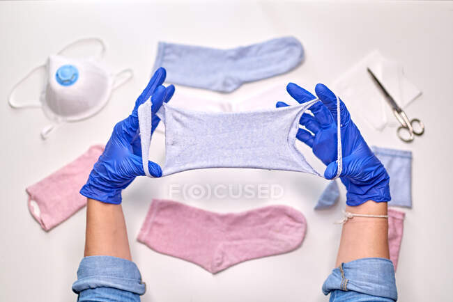Personne anonyme en gants bleus stériles montrant comment fabriquer un masque facial à l'aide de chaussettes tout en étant à la maison pendant la période de quarantaine du coronavirus — Photo de stock