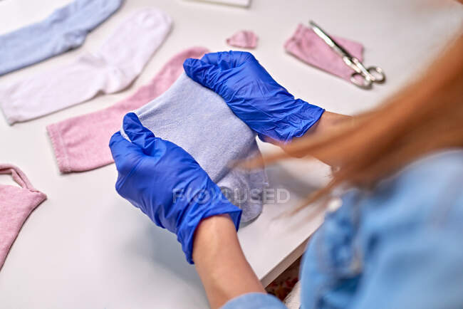 Persona anonima in guanti sterili blu che mostra come fare maschera facciale utilizzando calzini pur essendo a casa durante il periodo di quarantena coronavirus — Foto stock