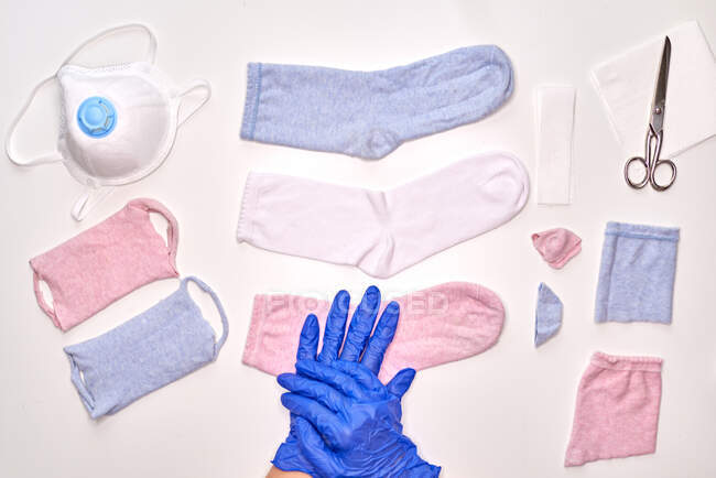 Анонімний чоловік у блакитних стерильних рукавичках показує, як робити маску обличчя за допомогою шкарпеток, перебуваючи вдома під час коронавірусного карантину. — стокове фото