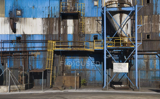 Esterno della fabbrica abbandonata con pareti metalliche blu e costruzioni e tubi metallici — Foto stock