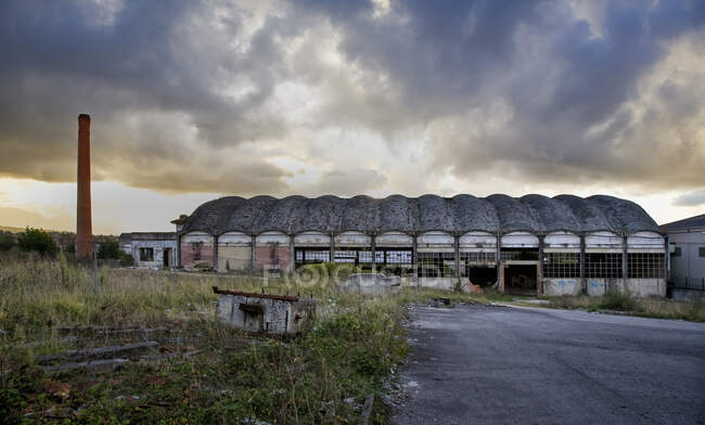 Solitario edificio industrial de piedra envejecida con paredes grises en mal estado situado entre arbustos verdes contra el cielo nublado en Asturias en España - foto de stock