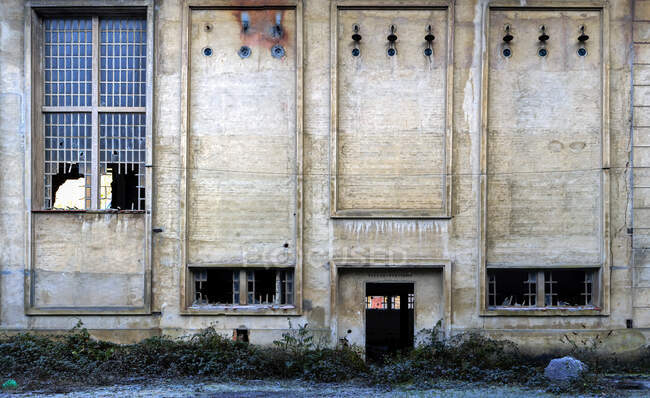 Exterior of abandoned stone industrial building with narrow windows with metal grid and broken glass — Stock Photo