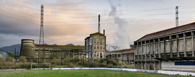 Широкий кут огляду старої покинутої фабрики з обшарпаними сірими будівлями та трубами, розташованими в іспанській сільській місцевості Астурії. — стокове фото