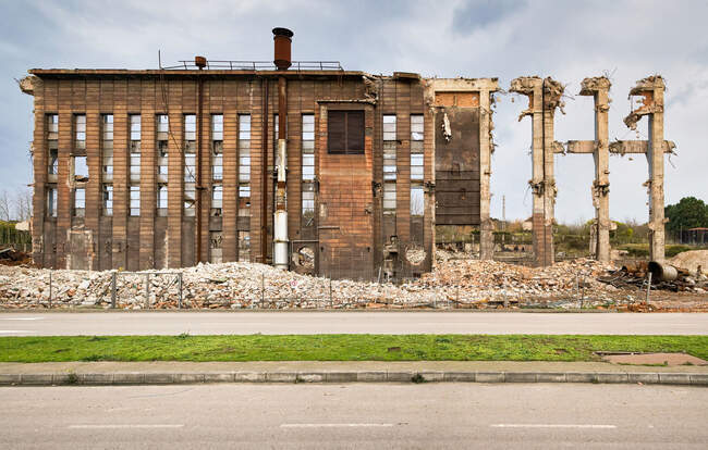 Ruinen alter Industriebauten mit Rohren und Müllbergen in Straßennähe vor bewölktem Himmel in Spanien — Stockfoto