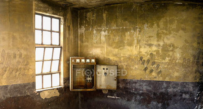 Vecchia scatola interruttore installata in un angolo della stanza stagionato con pareti in pietra squallida e finestra con griglia all'interno desolato edificio industriale — Foto stock