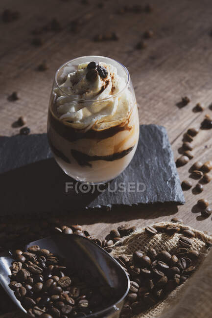 Glass of tasty cream coffee dessert with spoon served on black surface with coffee beans on wooden table — Stock Photo