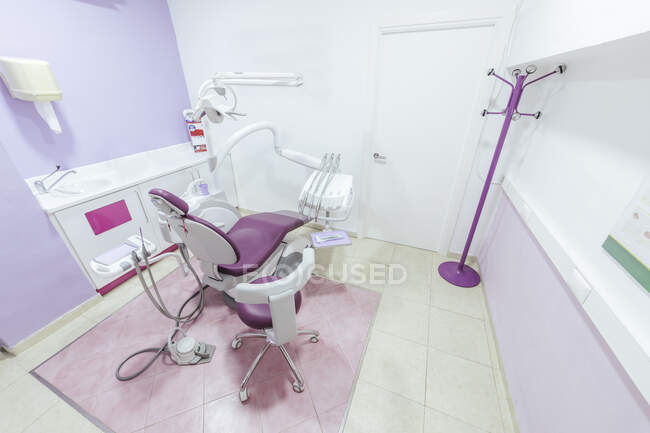Интерьер современного светлого пустого стоматологического кабинета со стулом и медицинскими инструментами и оборудованием, размещенными вокруг и белой раковиной возле стены — стоковое фото