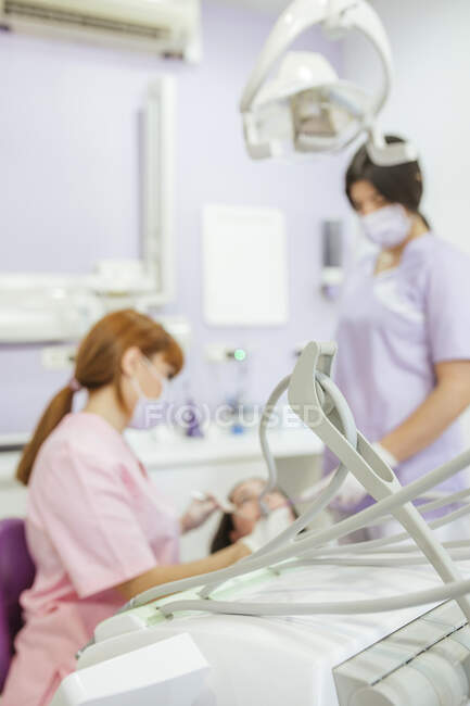 Женщина-стоматолог в форме и маске вылечивает зубы пациентки с ассистенткой в современной стоматологической клинике — стоковое фото