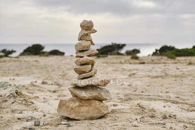 Камені, розміщені один на одному на порожній піщаній землі з морем на фоні — стокове фото
