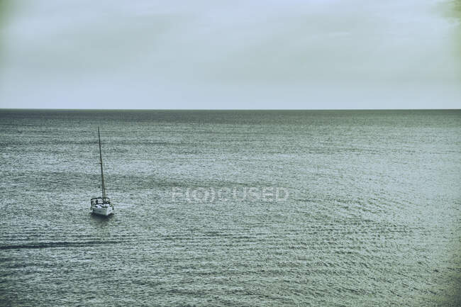 Белая яхта, плывущая по спокойным волнам голубого океана в пасмурный день на Ибице — стоковое фото