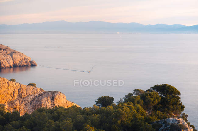 Schiff bewegt sich auf dem Meer mit fernen Bergen und Klippen im Sonnenuntergang — Stockfoto