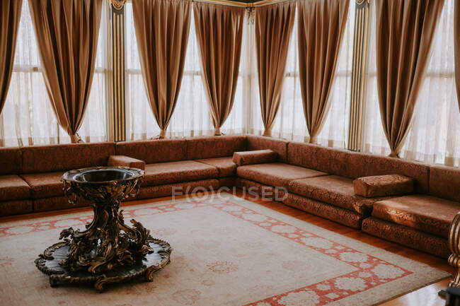 Spacious bright room with windows over comfortable sofas locating around perimeter of room with Turkish woven carpet and authentic forged vessel in middle of room in Istanbul — Stock Photo