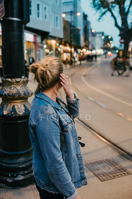 Vista laterale della donna bionda irriconoscibile in abito casual in piedi sulla strada e guardando lontano mentre si prepara attraversando la strada — Foto stock