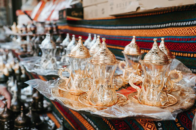 Conjunto de bules de vidro turcos tradicionais com ornamentos dourados compostos em bandeja em tecido oriental estampado no mercado em Istambul — Fotografia de Stock