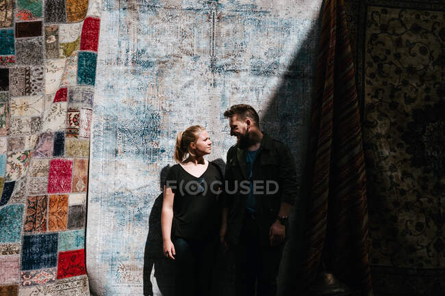 Joyful laughing couple hugging looking at each other and standing against background of ornamental turkish carpets in market in Istanbul on daytime — Stock Photo