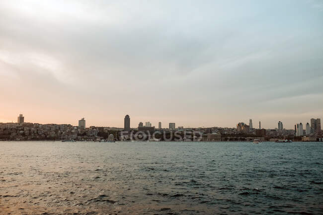 Picturesque scenery of remote city with skyscrapers locating near stunning sea and purple sunset sky with fluffy clouds in evening — Stock Photo