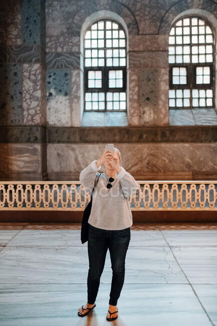 Серьезный женщина в повседневной одежде с шлепанцами стоя и фотографируя на смартфоне во время осмотра достопримечательностей Стамбула — стоковое фото