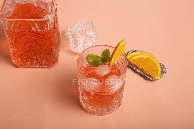 Сверху бокал свежего холодного коктейля с кубиками льда и мятой помещен на красочном фоне с ломтиками спелого апельсина — стоковое фото