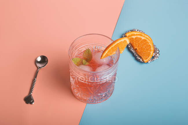Top view of alcohol cocktail with ice cubes and sprig of mint in glass placed on colorful background with orange slices — Stock Photo