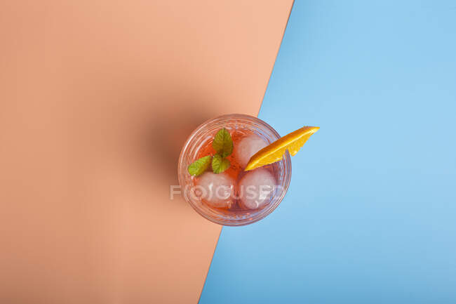 Вид зверху на алкогольний коктейль з кубиками льоду і гілочкою м'яти в склі, розміщеному на барвистому фоні з апельсиновим скибочкою — стокове фото